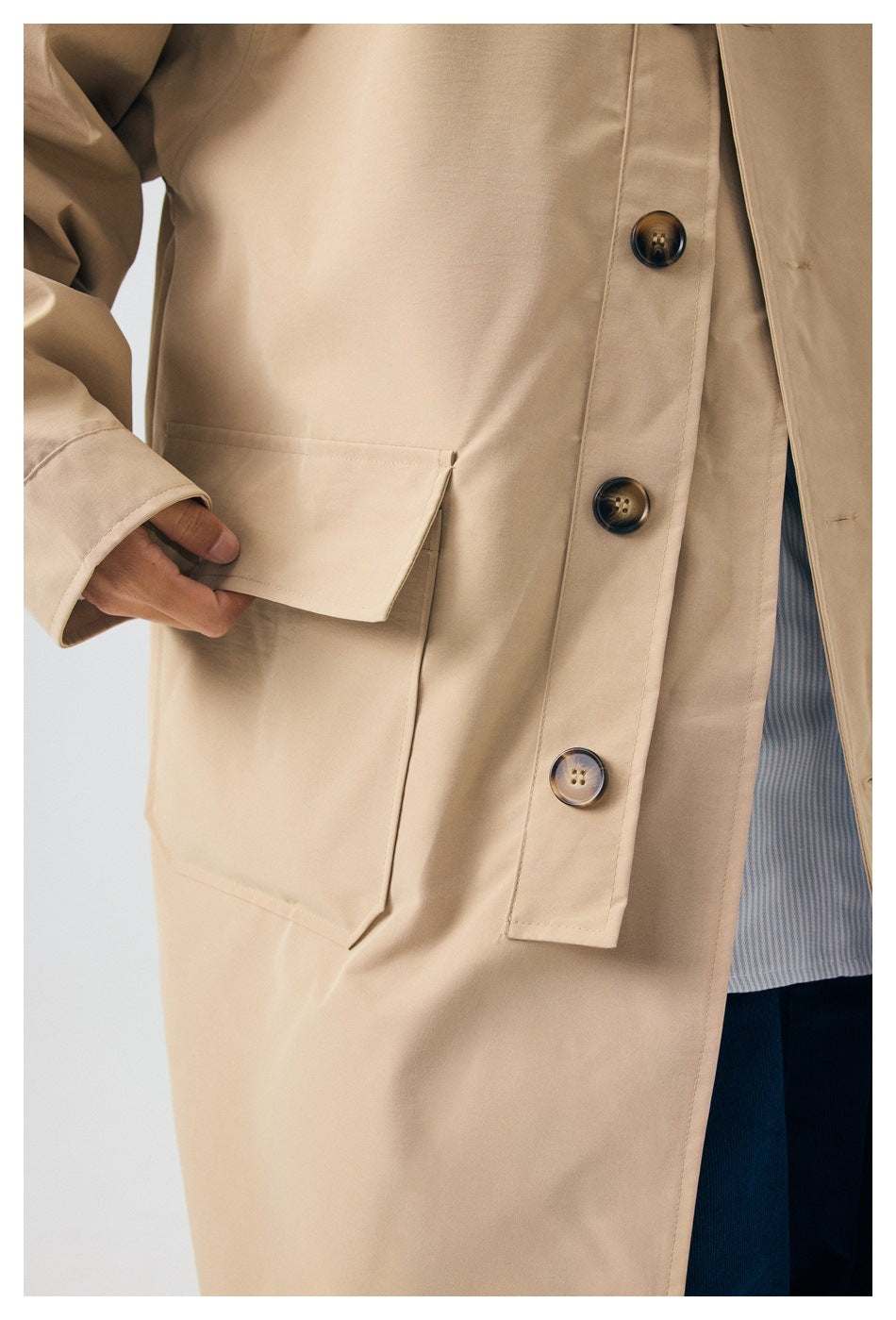 Close-up of the beige coat’s large flap pocket and row of dark buttons.