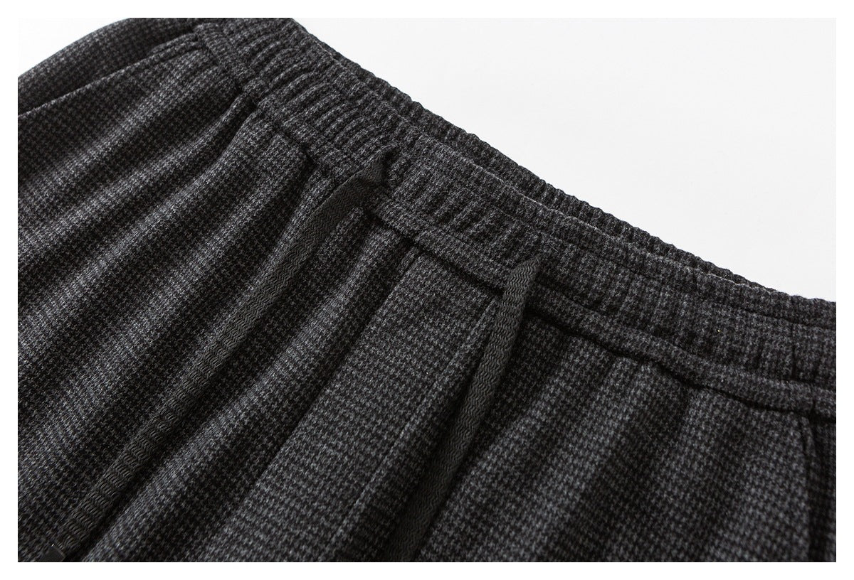Close-up of charcoal gray patterned trousers showing the elastic waistband, drawstring, and pleats.