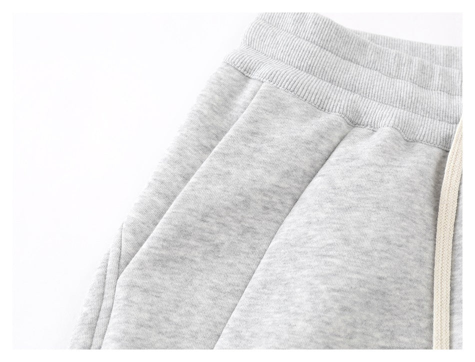 Close-up of light gray melange pants showing the waistband, side seam, and one cream drawstring.