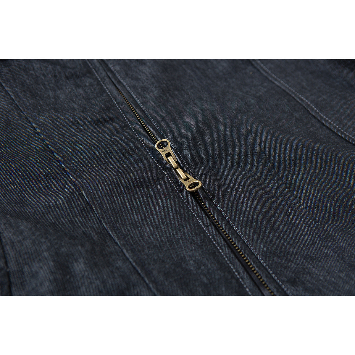 Close-up of the dark indigo jacket's zipper, brass-colored double pull, and contrast stitching.