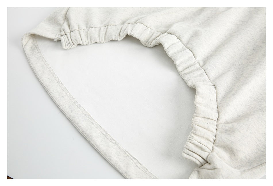 Close-up of a gathered elasticized edge and stitched seam on light gray heather fabric.