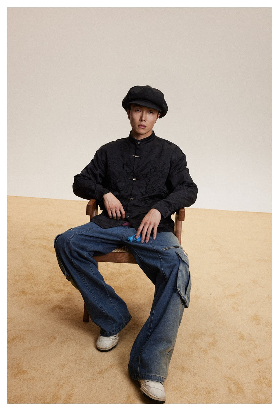 Seated model wearing a black textured jacket with frog closures and tonal embroidery on the front.