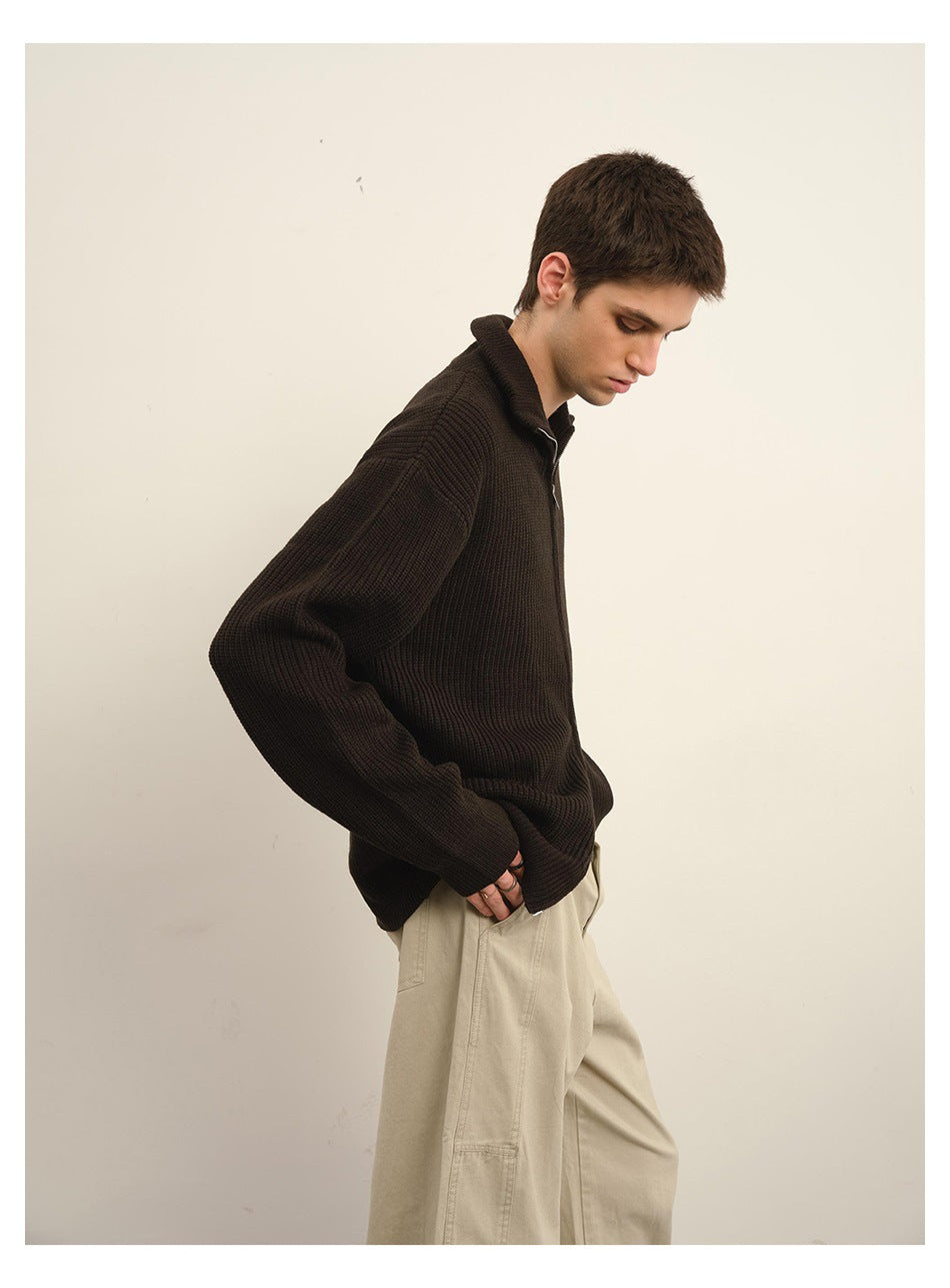 Side view of a model wearing a dark brown ribbed zip-front sweater with a high collar and beige trousers.
