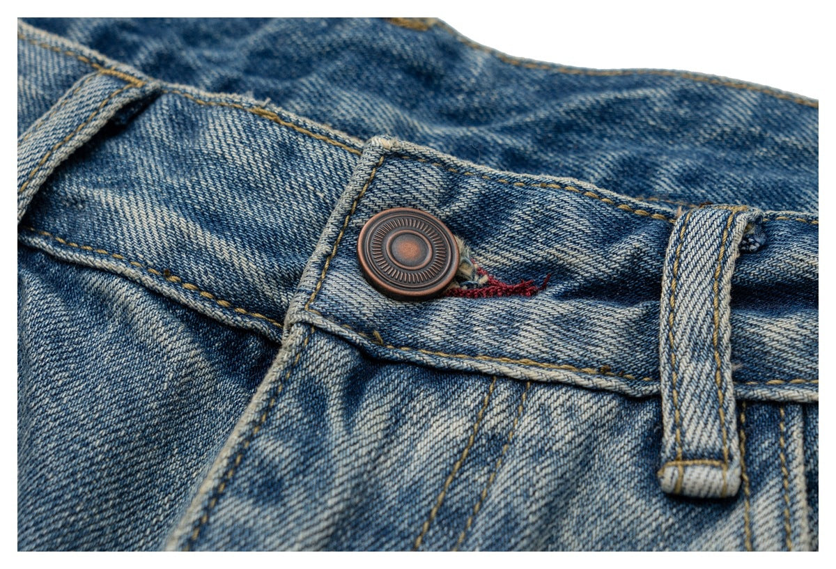 Close-up of faded blue jeans showing the waistband button, belt loop, and gold stitching.