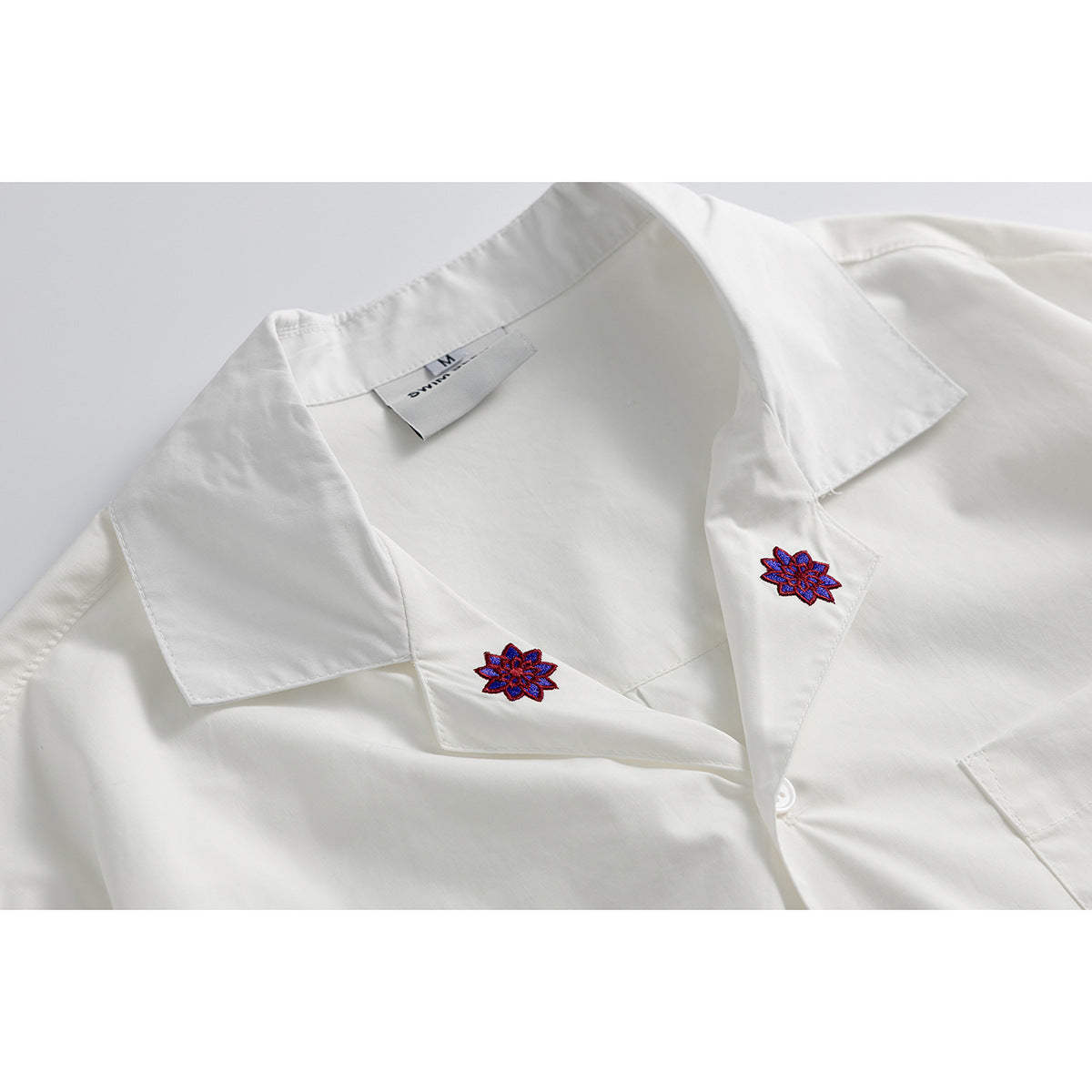 Close-up of a white shirt collar with purple and red floral embroidery on the lapels and a neck label.