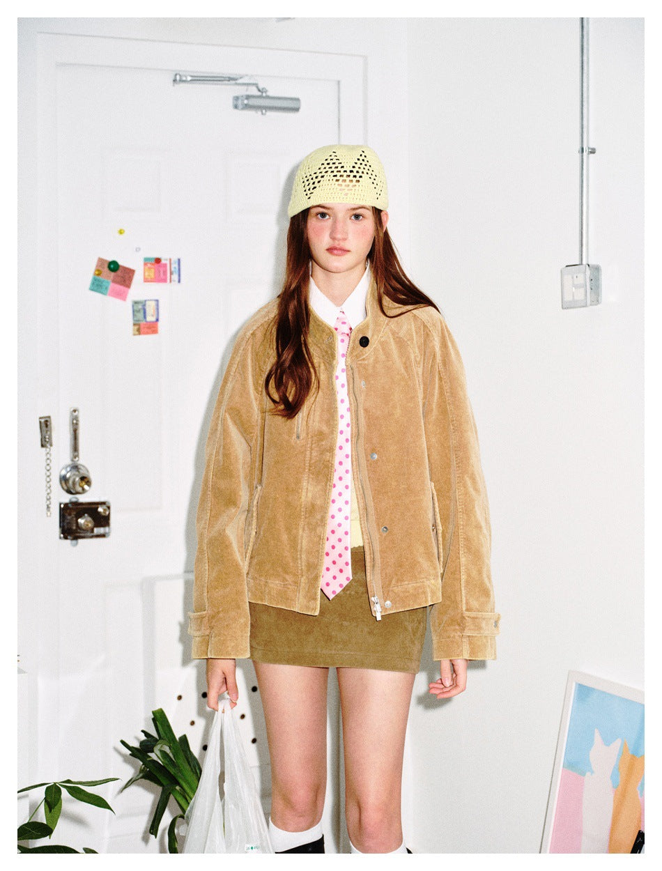 Model wearing an open khaki corduroy jacket with a pink polka dot tie, cream beanie and tan mini skirt