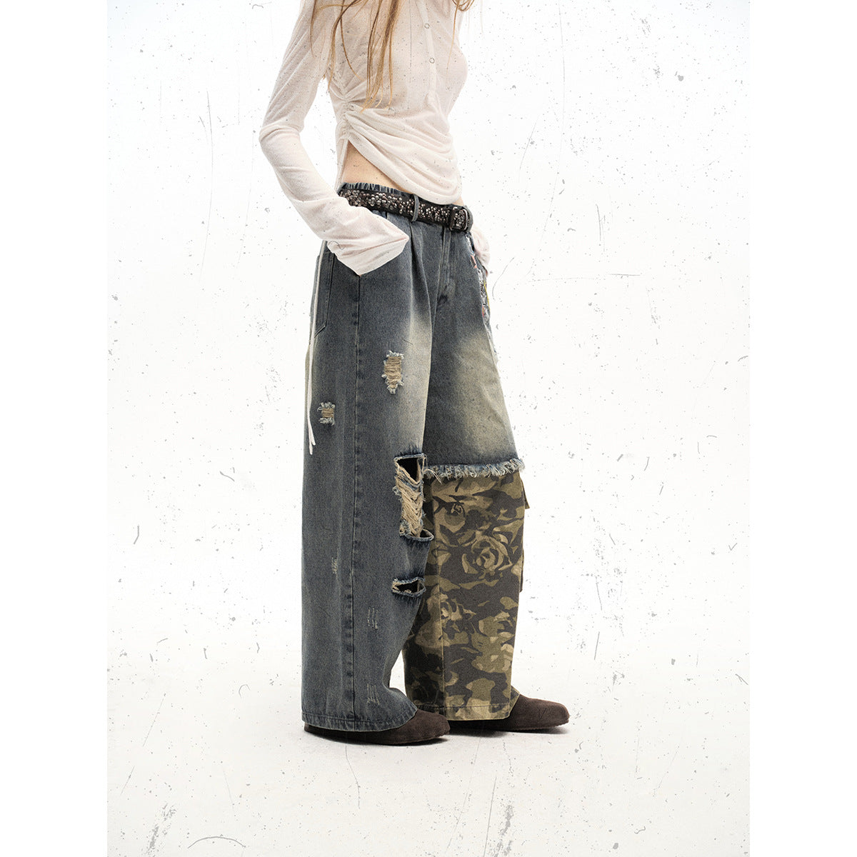 Angled side view of a model wearing wide-leg gray jeans with distressed details and a camouflage cargo panel.