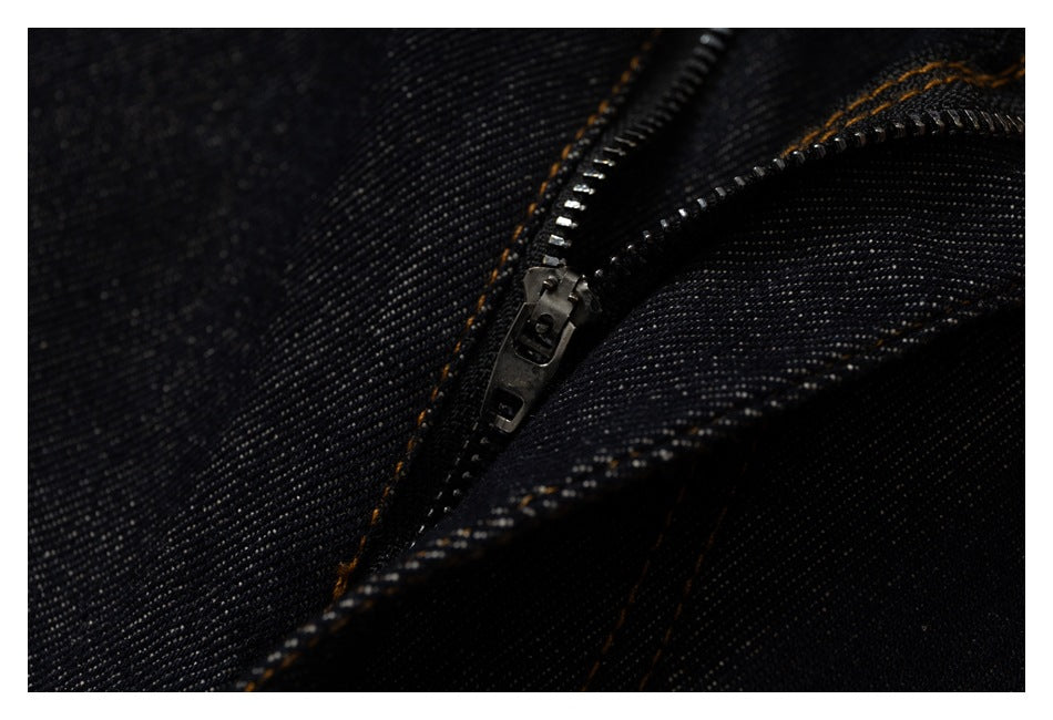 Extreme close-up of a dark metal zipper and orange-brown stitching on black denim pants.