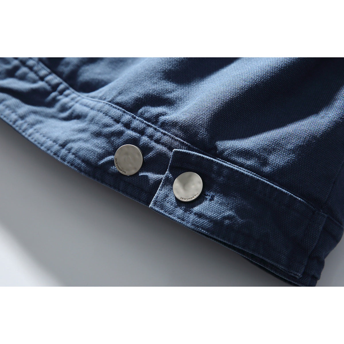 Close-up of the blue jacket hem showing two round metal buttons and textured fabric.
