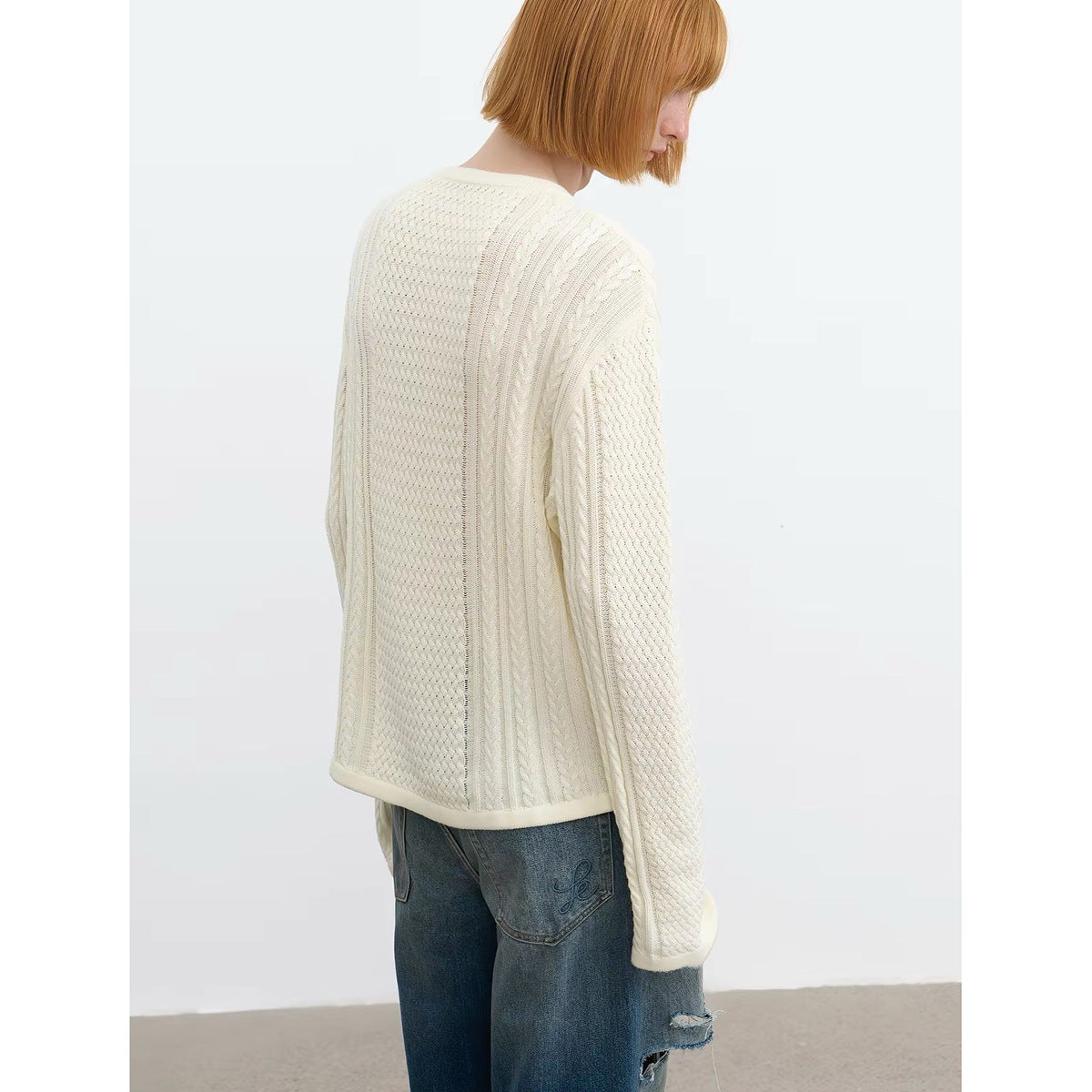 Back view of a model wearing an ivory textured knit pullover and blue jeans.