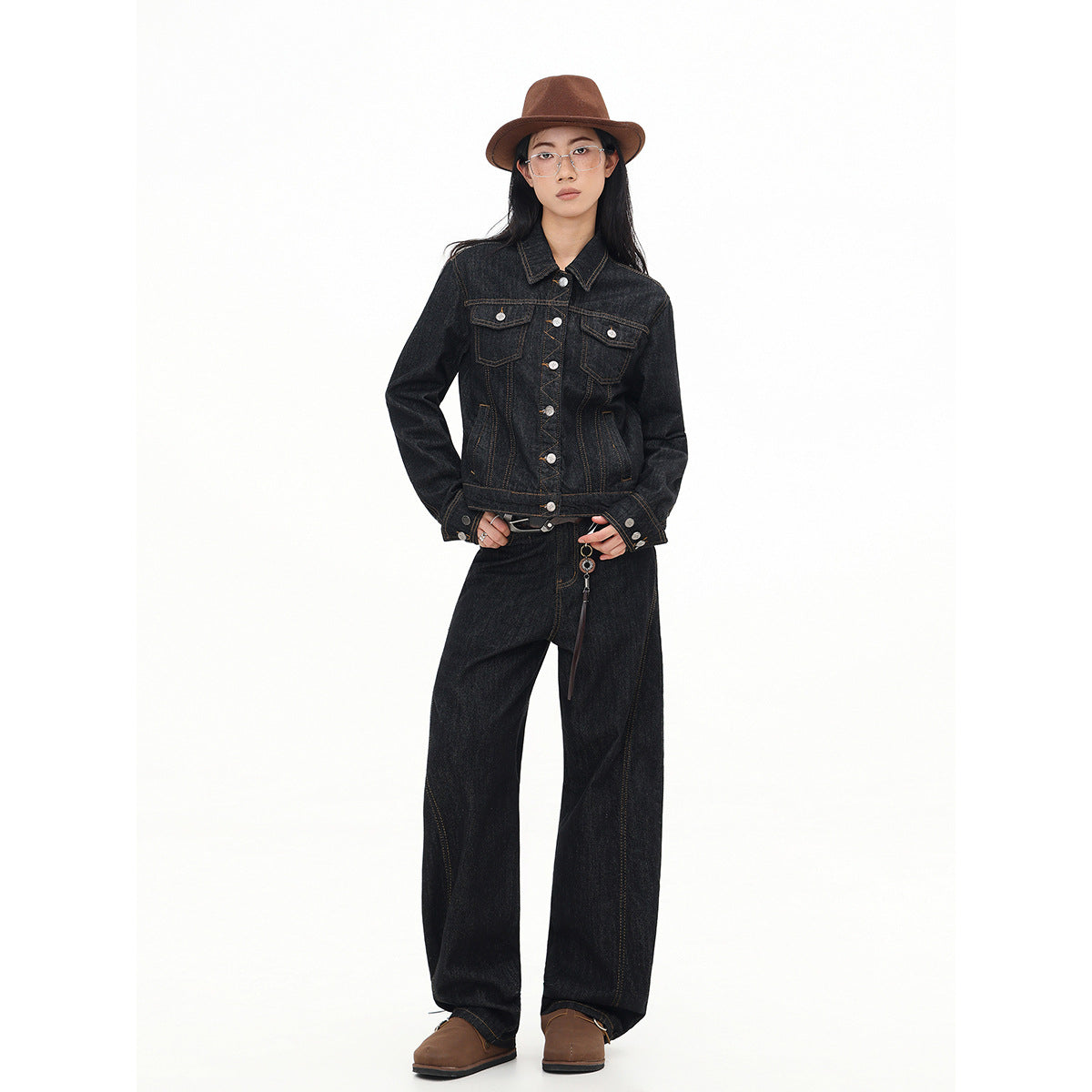 Full-length front view of a model wearing a black denim jacket and wide-leg jeans with brown contrast stitching.