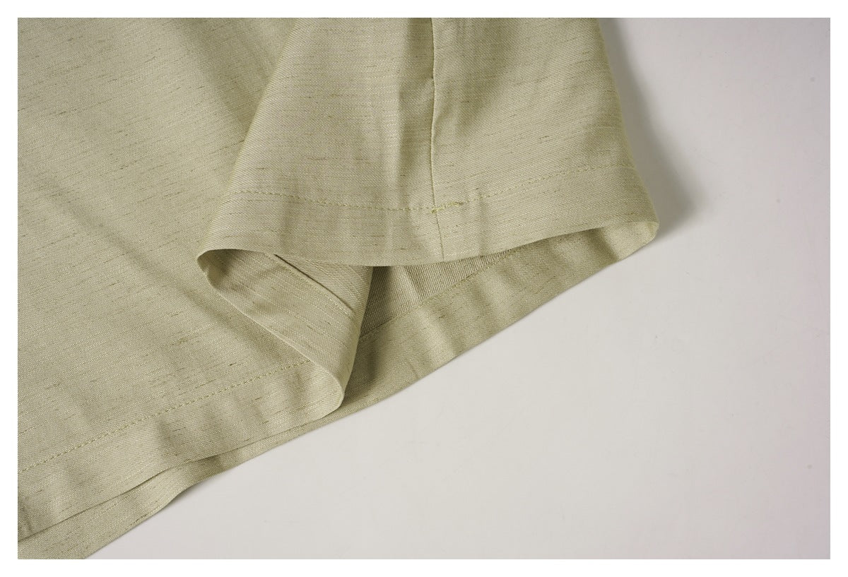 Close-up of a pale olive-beige garment's folded, stitched hem against a light background.
