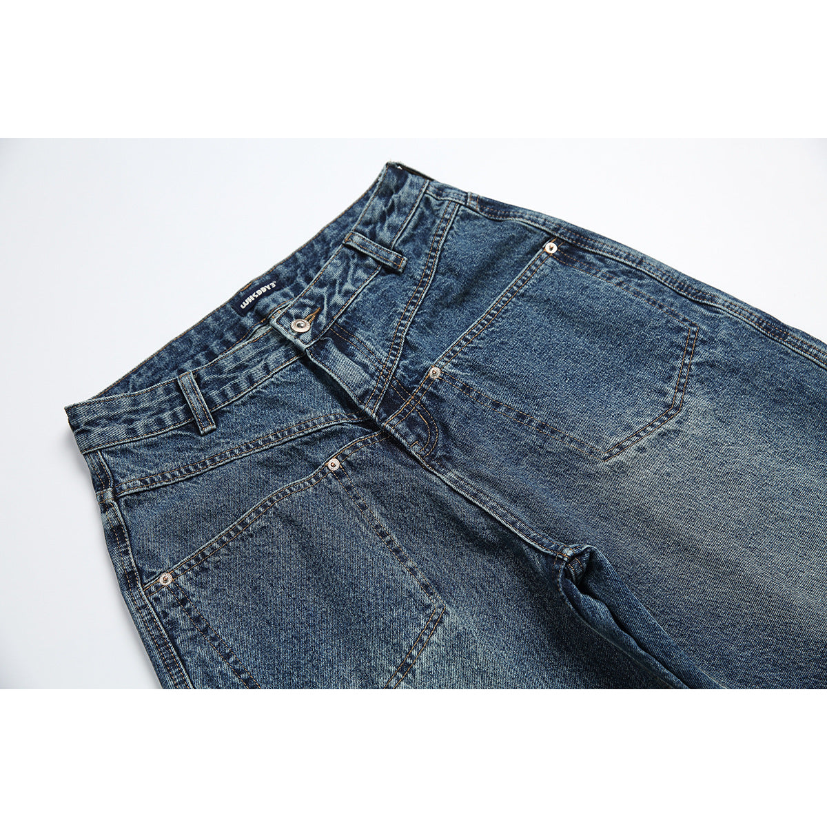 Close-up of blue-wash jeans showing the front waistband, belt loops, button, and pocket details.