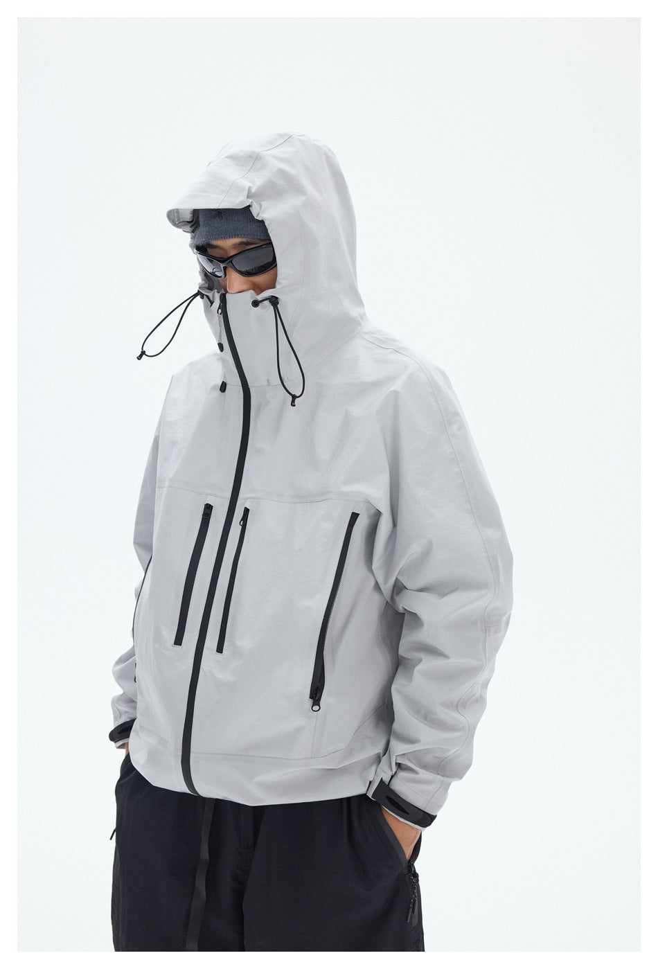 Close view of a man wearing a light gray hooded jacket with black drawcords and multiple zip pockets.