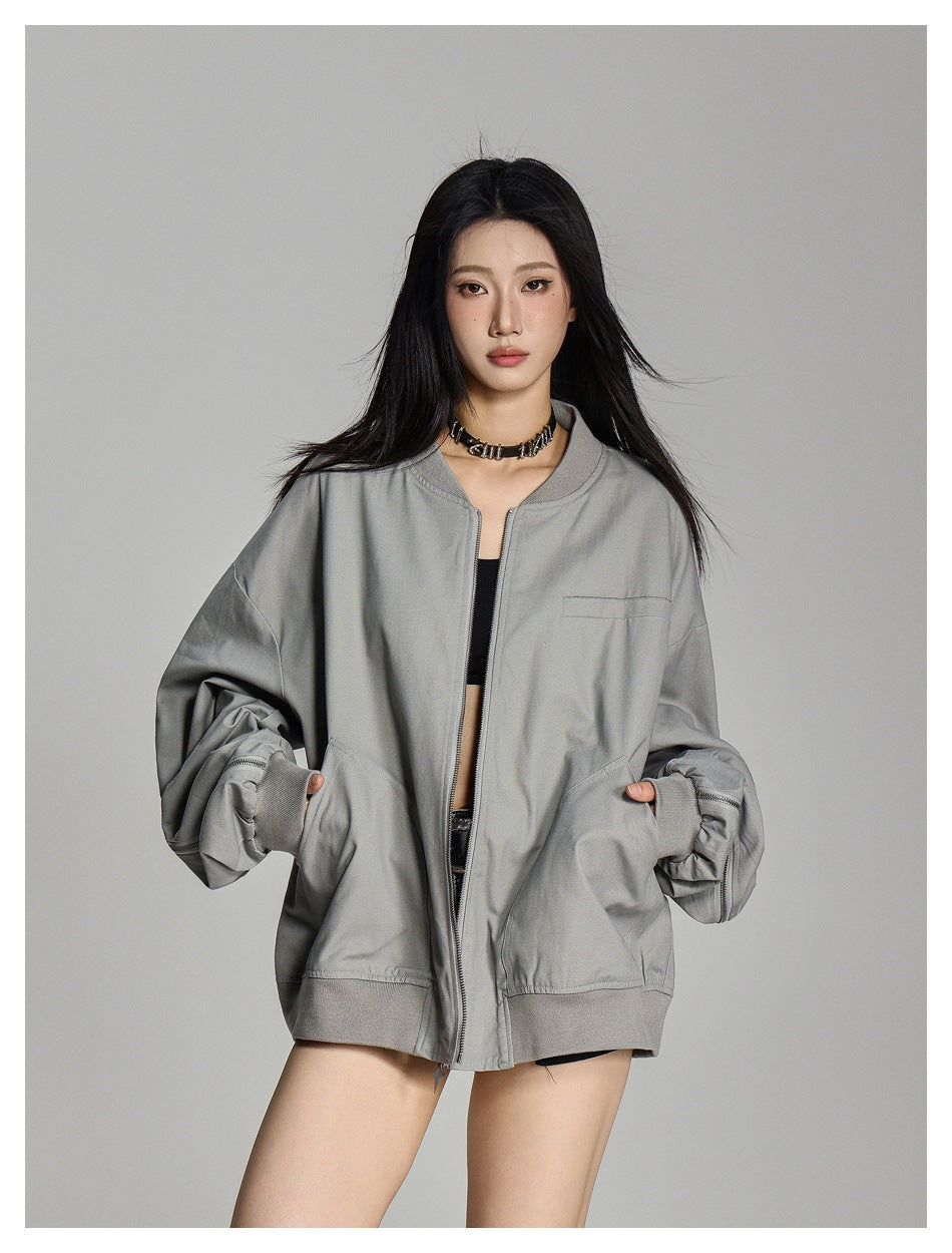 Model wearing a light gray oversized zip jacket with hands in its curved front pockets and the sleeves gathered at the cuffs.