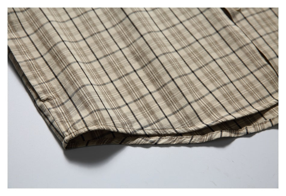 Close-up of the curved hem and stitching on a beige plaid shirt.