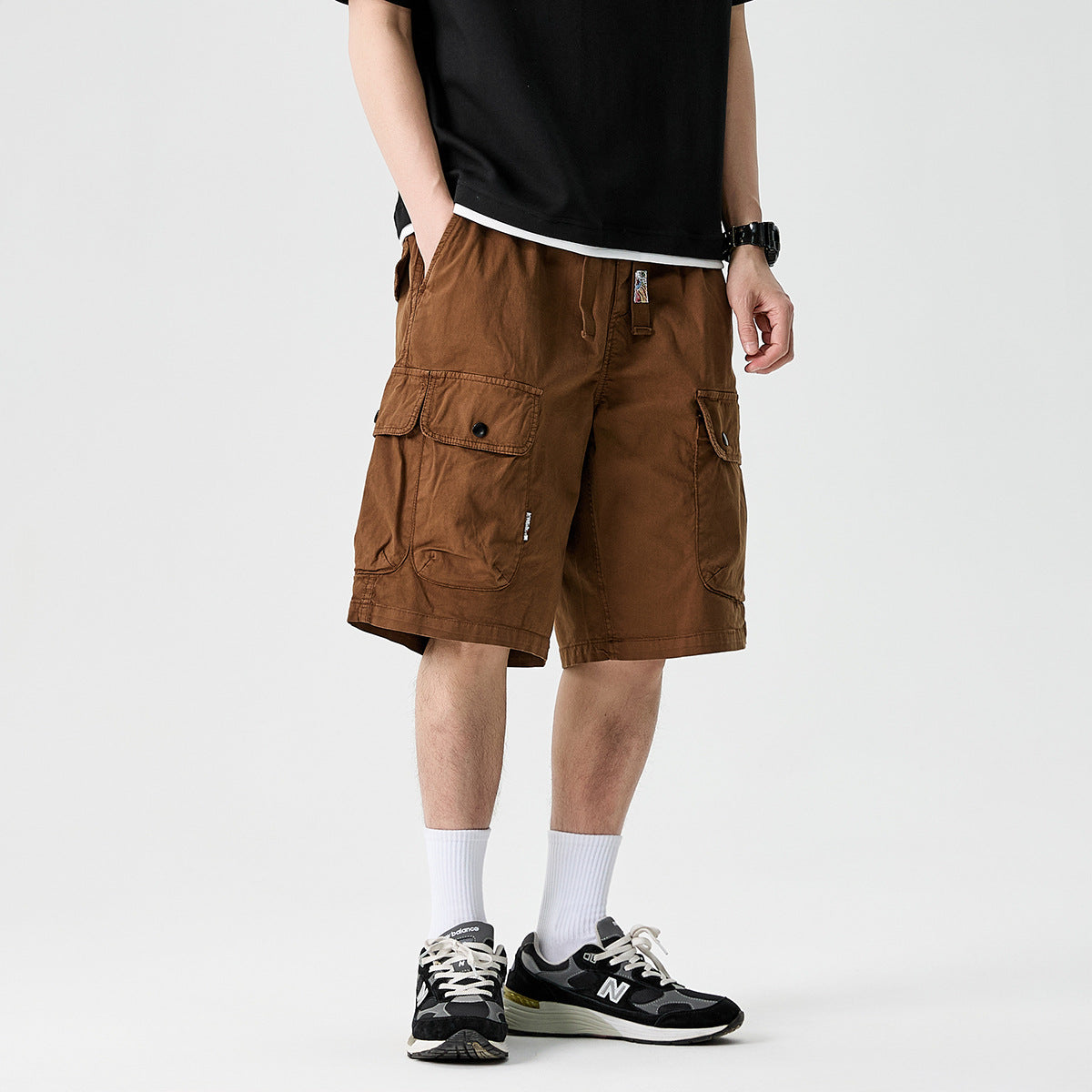 Cropped model wearing brown cargo shorts with oversized flap pockets and a black T-shirt.