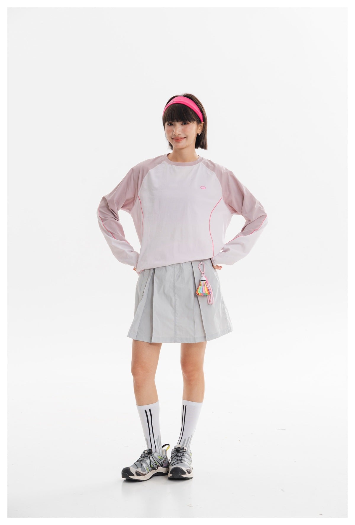 Model wearing a pale pink and white long-sleeve top with a light gray pleated skirt.