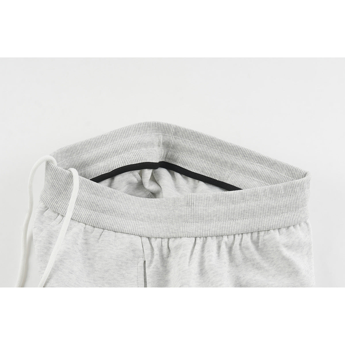 Close-up of light gray shorts showing the ribbed waistband, white drawstring, and black inner trim.