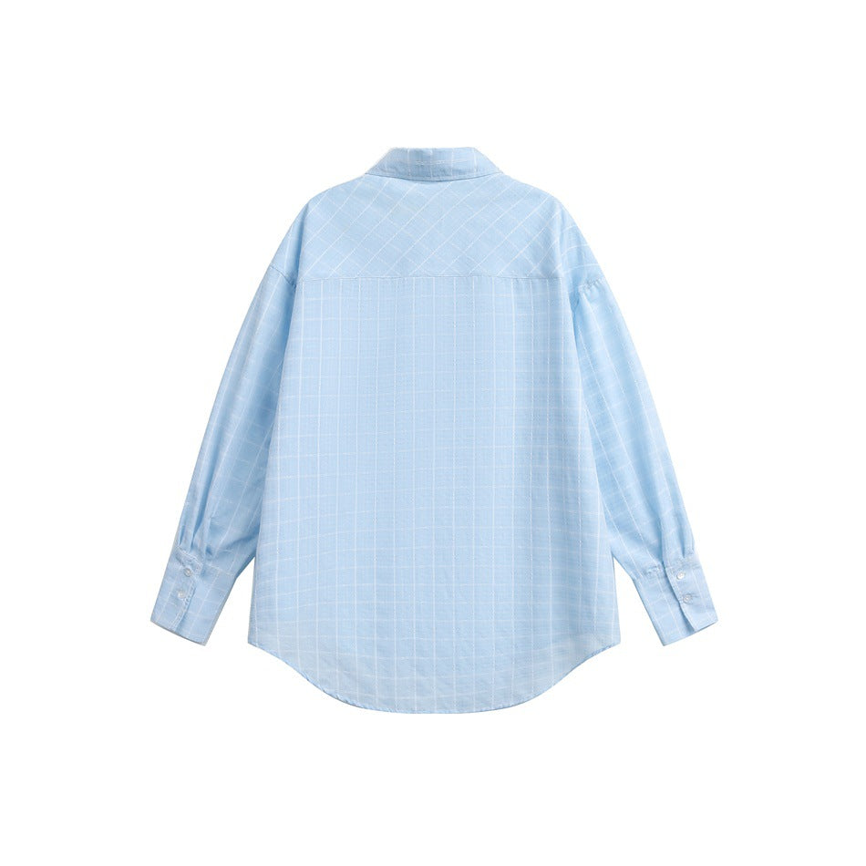 Flat lay of a light blue windowpane-check shirt, showing its back, collar, long sleeves and curved hem.