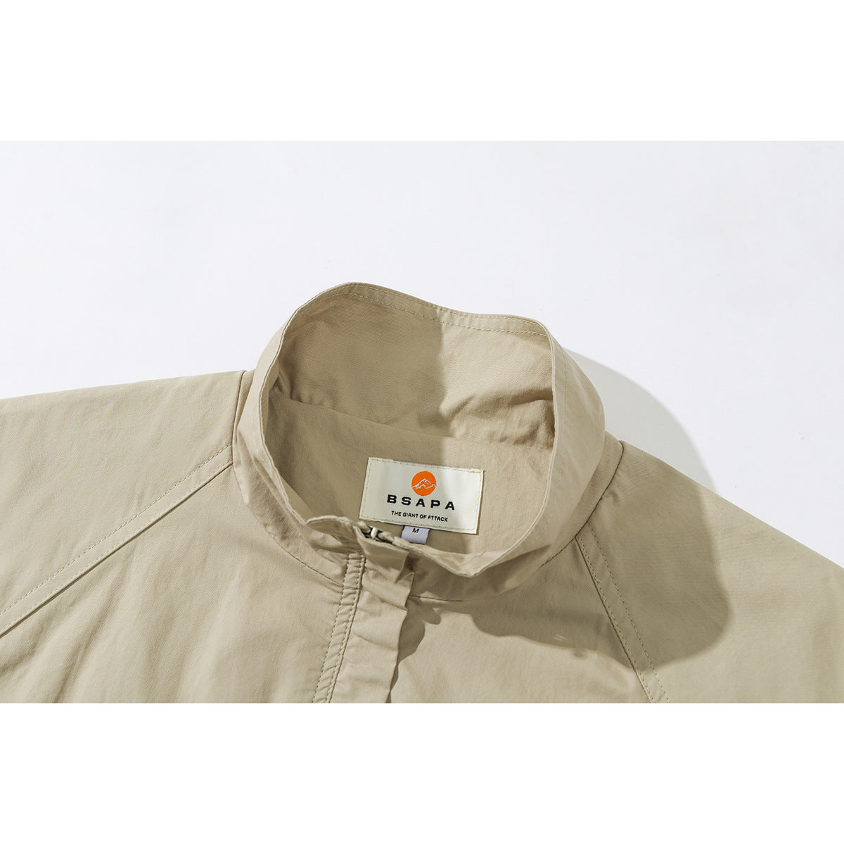 Close-up of a beige jacket's stand collar, covered front fastening, shoulder seams and sewn neck label.