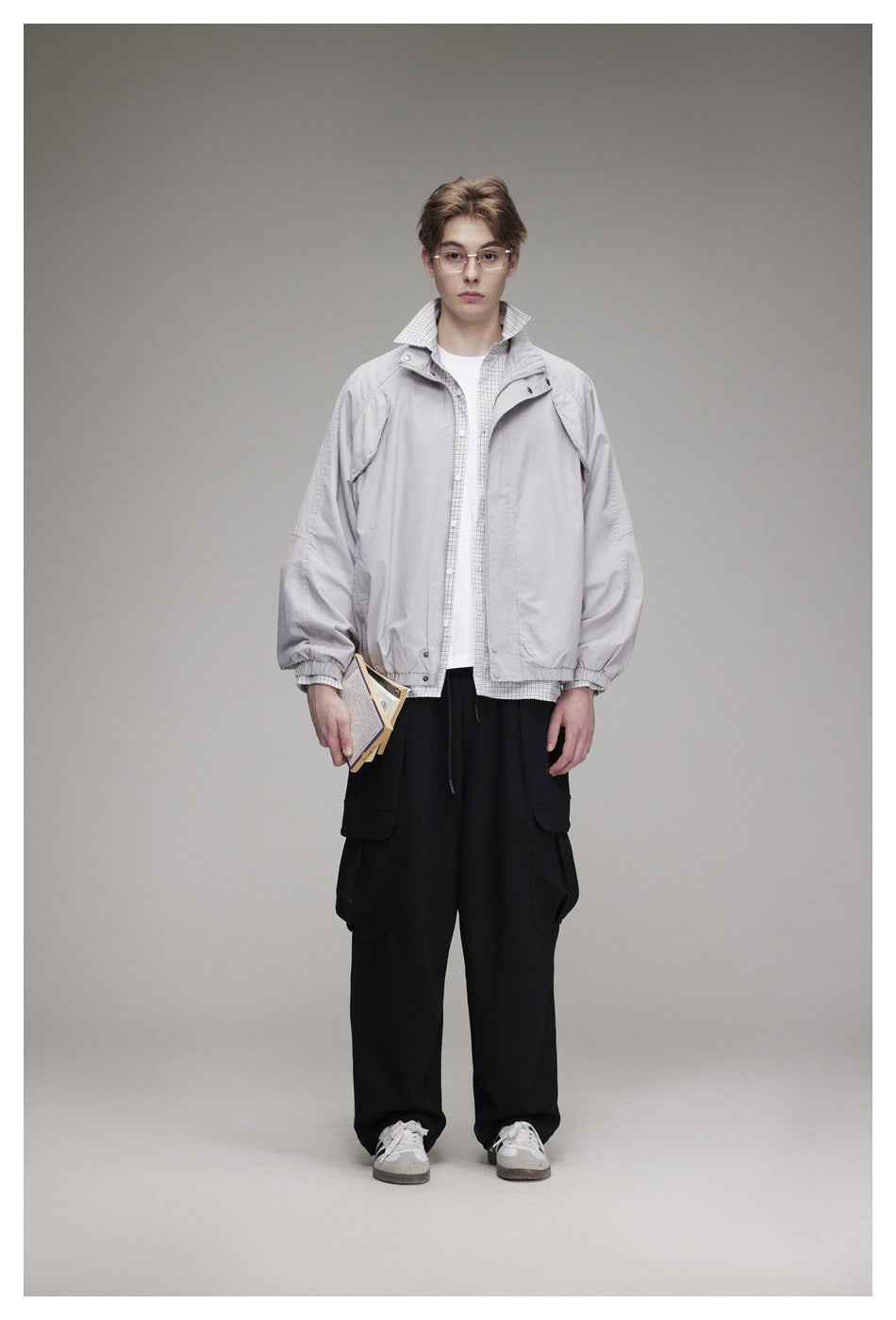 Model wearing a light gray stand-collar jacket over a checked shirt and white tee with black cargo pants, front view