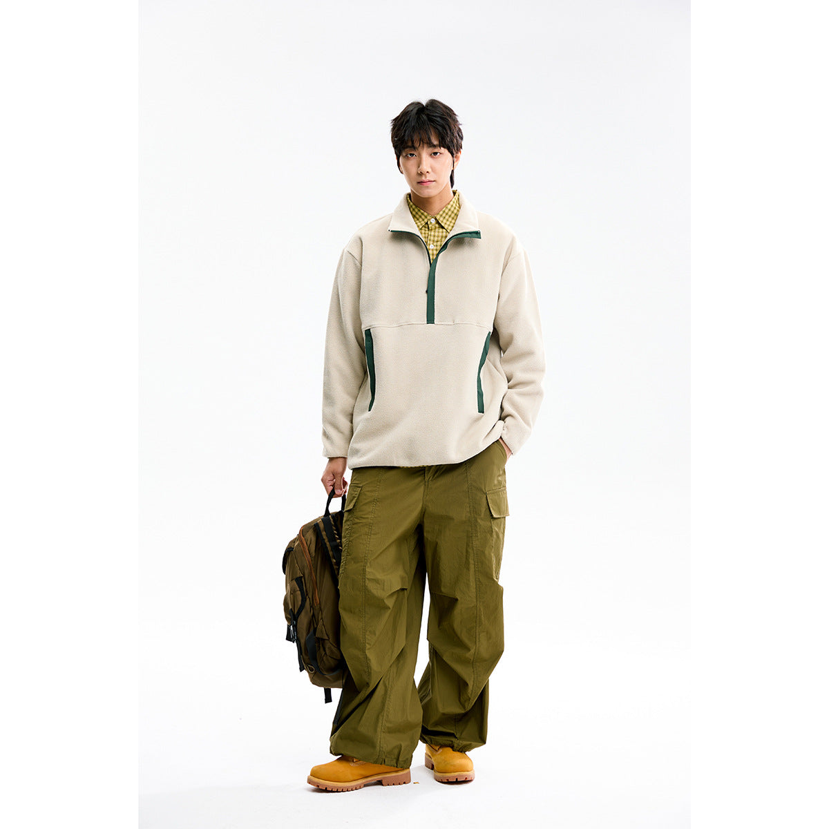 Front view of a model in a cream pullover with dark green trim, yellow checked shirt, and olive cargo pants.