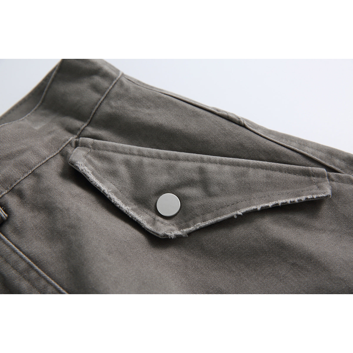Close-up of a gray shorts pocket flap with a round snap button and visible stitching.