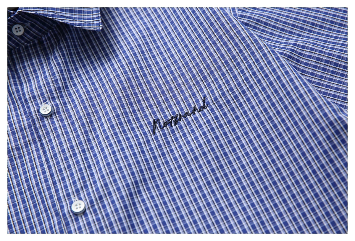 Close-up of a blue checked shirt front with white buttons and black embroidered script.