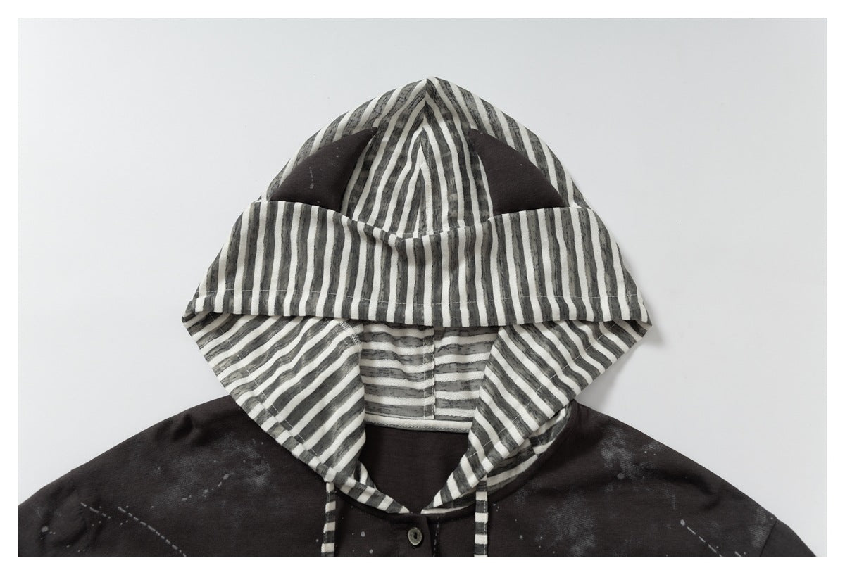 Upper front of a dark hooded garment with a striped hood lining and drawstrings, pale scattered markings, and a button.
