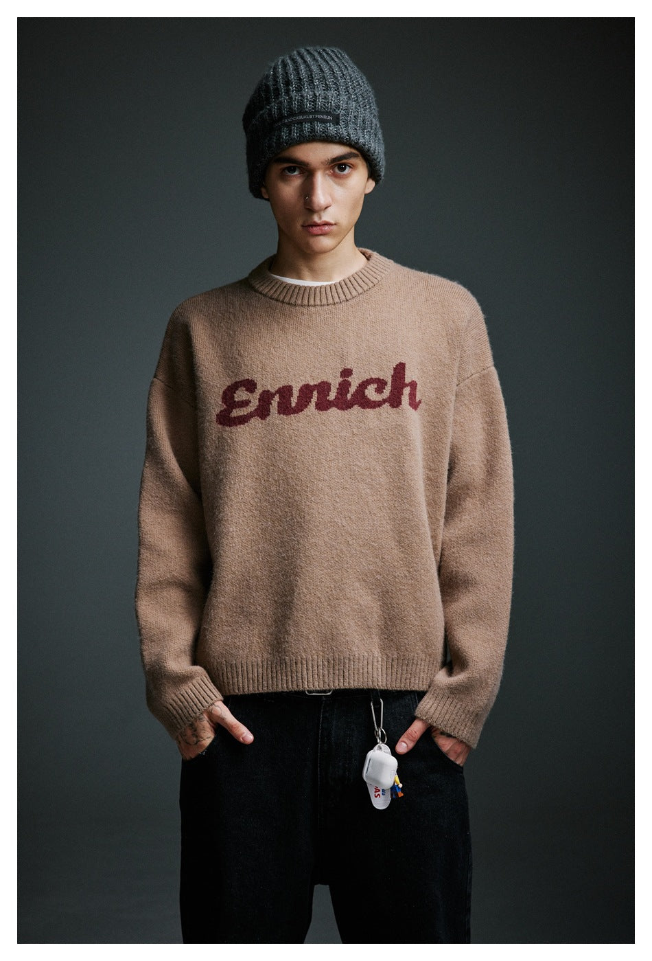 Model wearing a taupe crewneck sweater with burgundy script lettering and a dark gray rib-knit beanie.