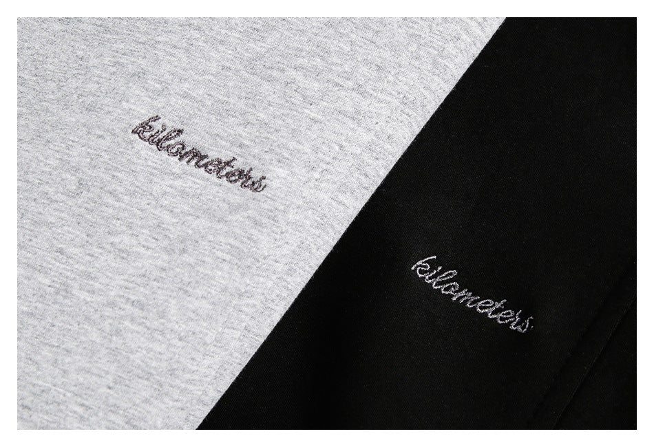 Close-up of small cursive embroidery on light gray and black sweatshirt fabric.