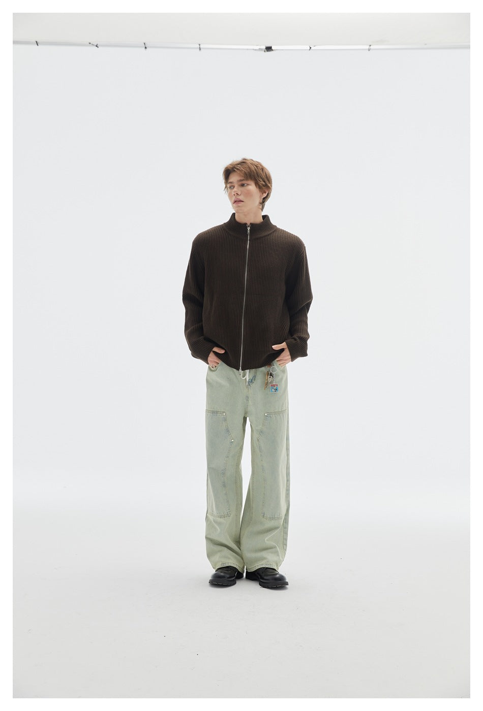 Full-length model wearing a dark brown ribbed cardigan with a front zipper and pale green wide-leg jeans.