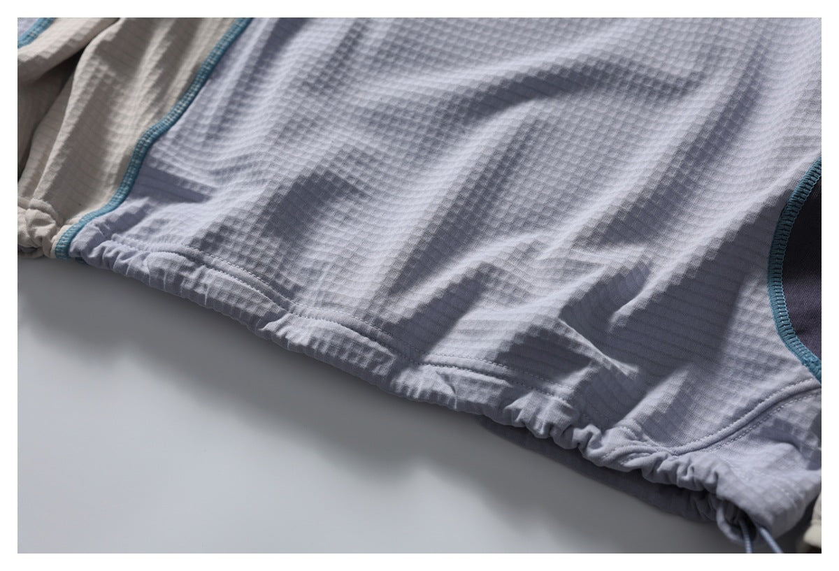 Close-up of a gray textured garment hem with gathered stitching and teal-trimmed panel seams.