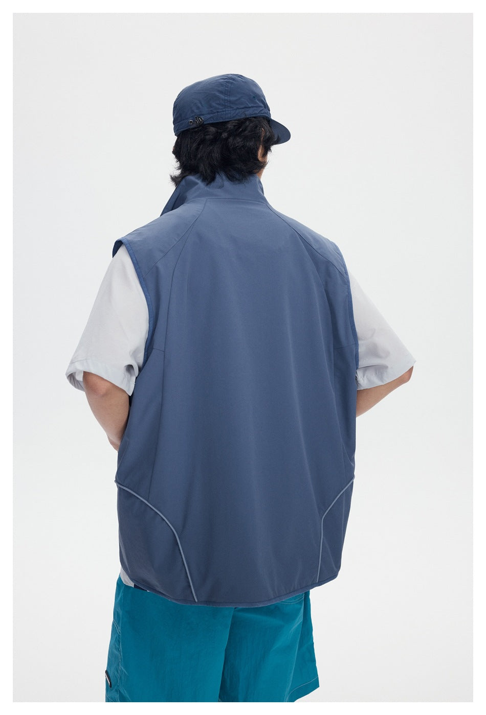 Rear view of a blue-gray sleeveless vest worn over a white T-shirt, with turquoise shorts.