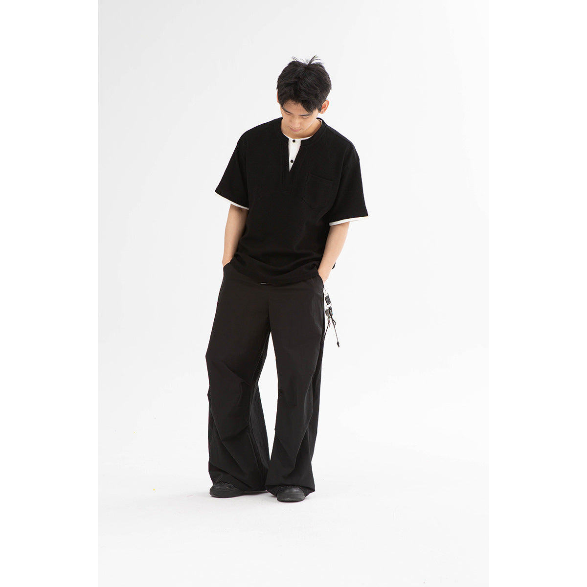 Model wearing a black short-sleeve split-neck shirt with white trim and a chest pocket, paired with wide-leg black pants.