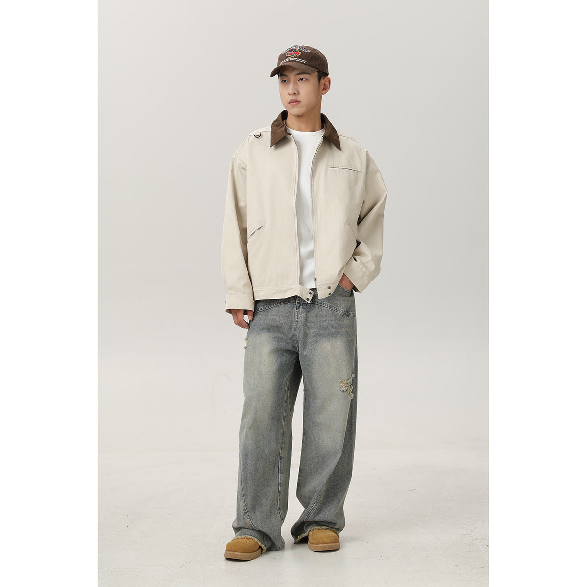 Full-length front view of a model wearing a cream jacket with a brown collar and loose distressed gray jeans.