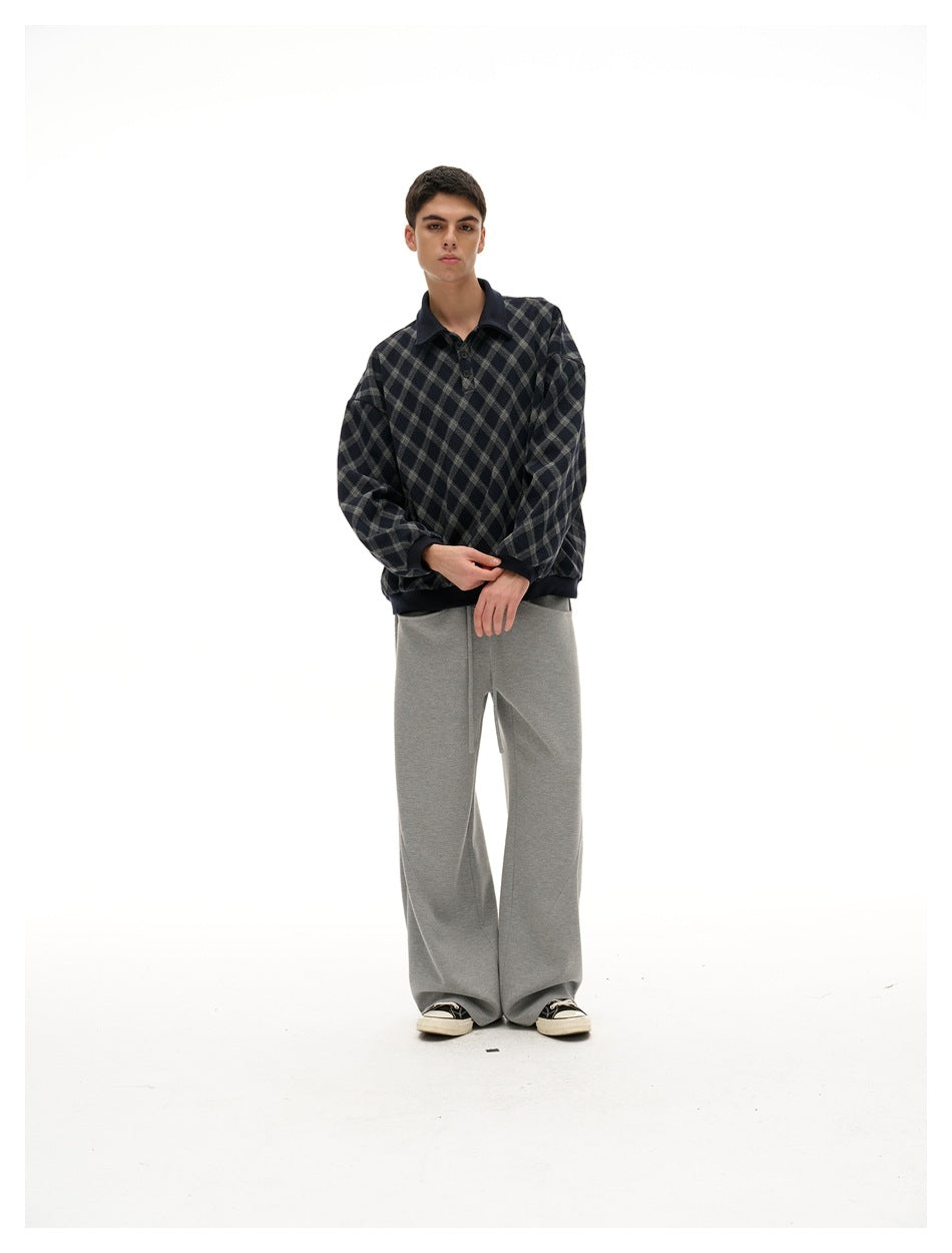 Full-length model wearing a navy and gray diamond-plaid pullover with a dark collar and gray wide-leg pants.