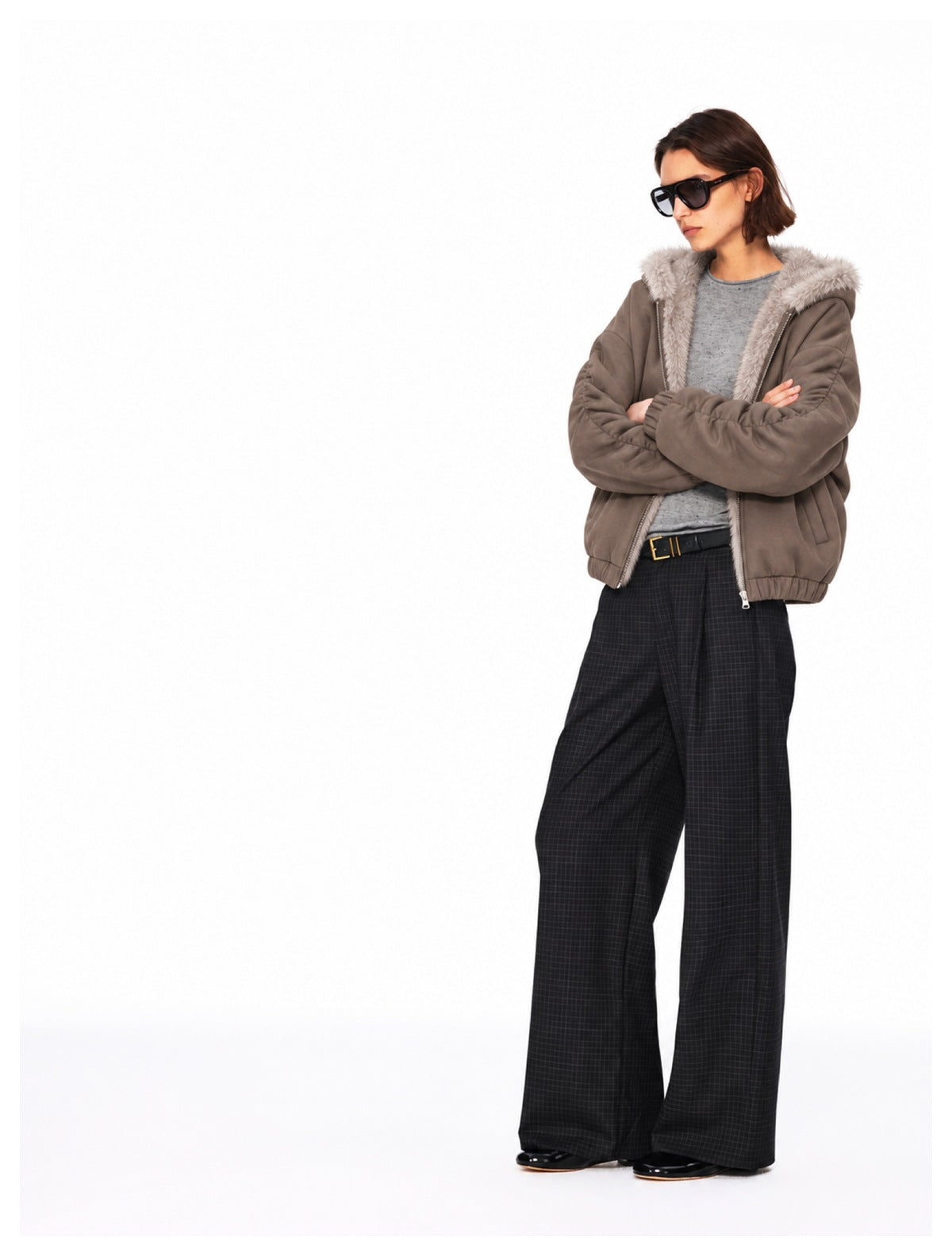 Model in a taupe fur-trimmed hooded jacket and wide-leg checked trousers, arms crossed.