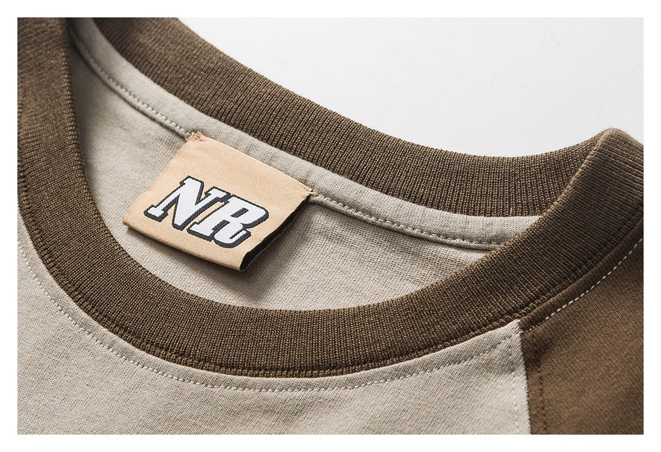 Close-up of a taupe crew-neck garment with a dark brown ribbed collar and tan neck label with stylized lettering.