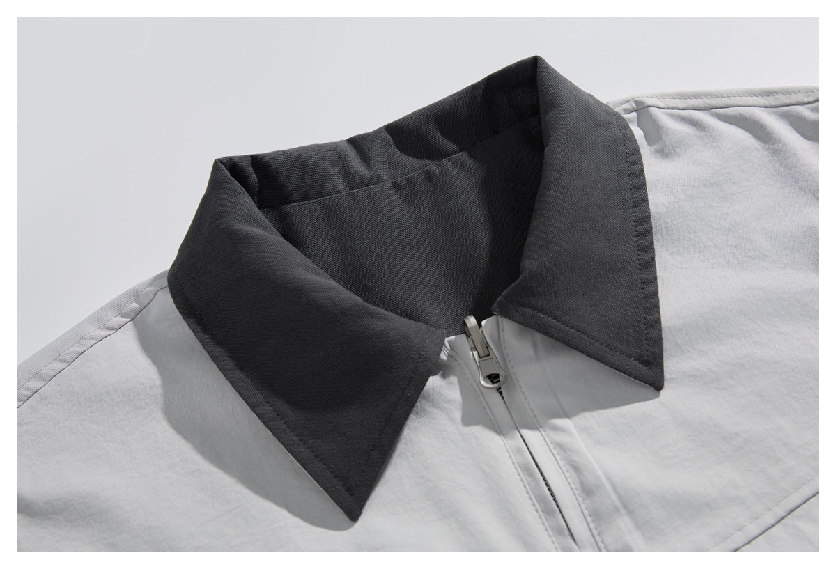 Close-up of a light gray jacket with a contrasting charcoal collar and front zipper.