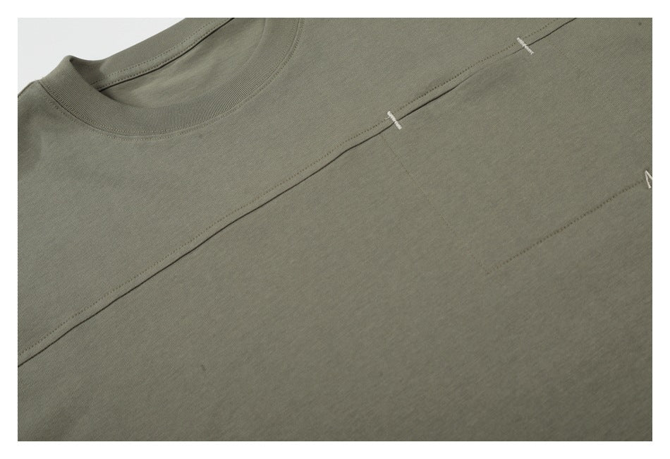 Close-up of a muted olive-gray T-shirt showing the neckline, chest panel seam, and small white stitch accents.