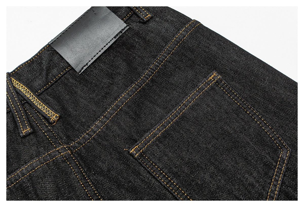 Angled close-up of a back pocket, waistband, belt loop and blank dark patch on black jeans.