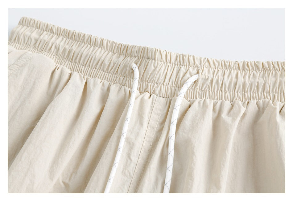 Close-up of cream pants showing the gathered elastic waistband, stitching, and white drawcords.