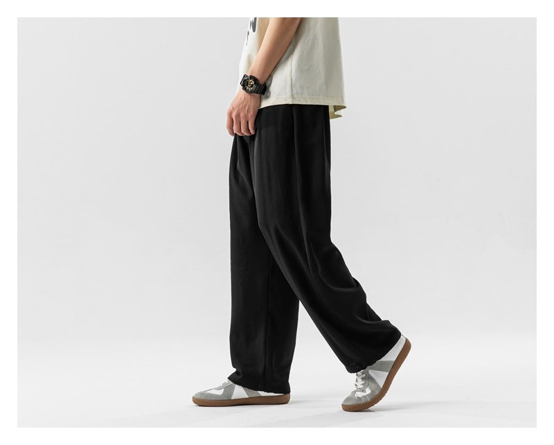 Side view of a model wearing loose black pants and gray sneakers.