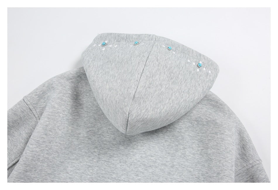 Close-up of a light gray hoodie back and hood, decorated with turquoise studs and small white embroidered dots.