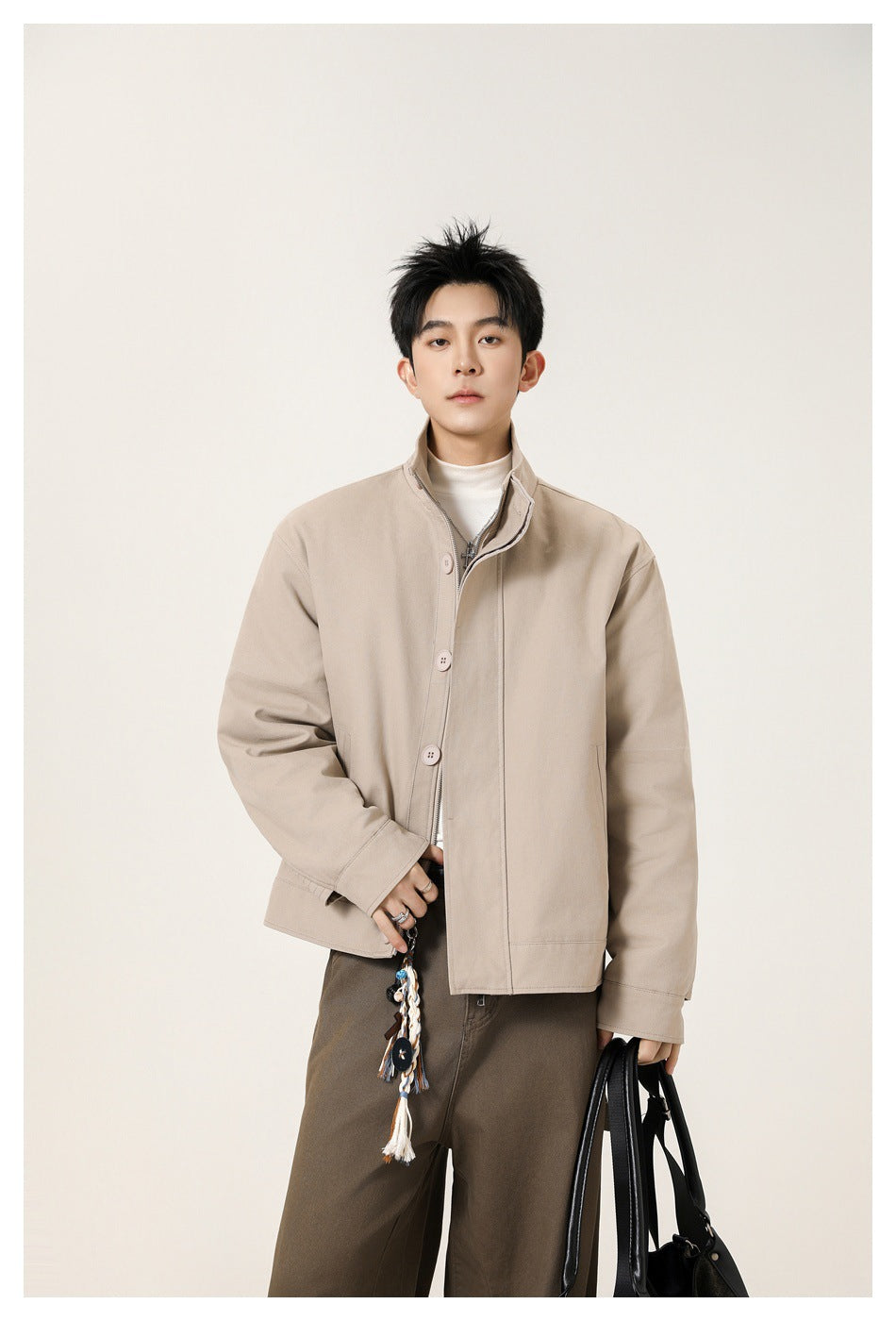 Model wearing a beige high-collar jacket with a button-and-zip front and brown trousers.