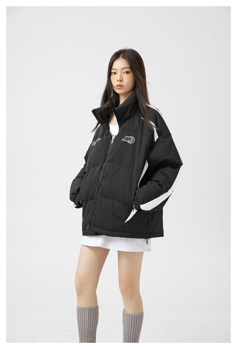Front view of a model wearing a black padded zip jacket with white sleeve panels and chest graphics.