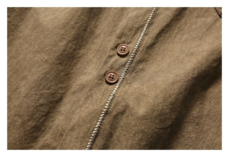 Close-up of two brown buttons and pale decorative stitching along the front of a brown shirt.
