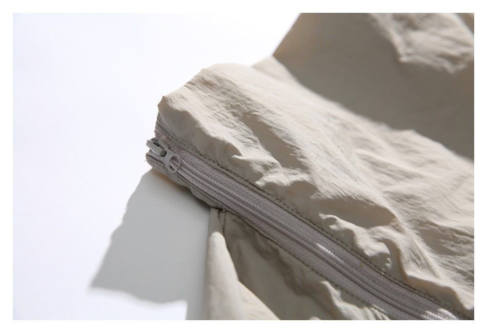 Close-up of the beige jacket's zipper slider and stitching along a curved seam.